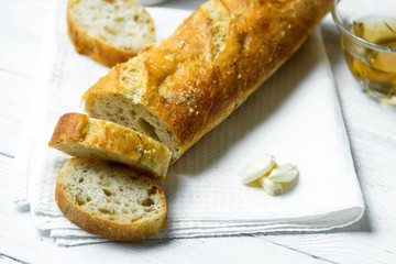 Garlic baguette on white kitchen towel on wooden table.