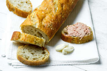 Garlic baguette with pate on white kitchen towel on wooden table.