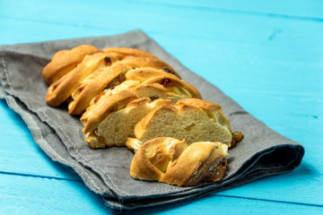 Piece of Sweet Braided Bread with raisins on kitchen towel on blue wooden background.