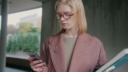 Nerd student cute girl in round glasses collecting information from web using mobile phone or smartphone checking publishing post on social network website or app reading digital book encyclopedia