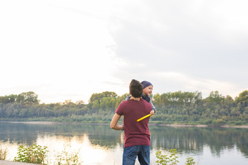 Family, happiness, people concept - father with son in his arms near the river