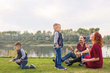 Family and nature concept - Mother, father and their children playing with colorful soap bubbles