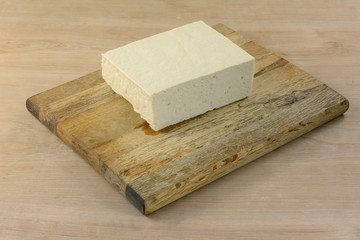 Block of extra firm tofu on cutting board to prepare for adding as ingredient to meal in cooking