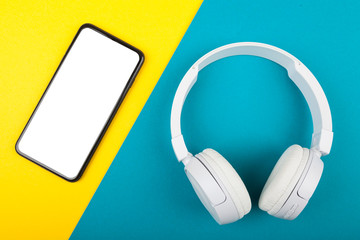 Smartphone, mobile phone with wireless white headphones on blue and yellow background. Ready to listen music.