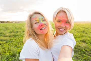 Indian festival of holi, people concept - two young woman taking selfie with colourful powder on the faces