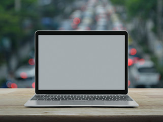 Modern laptop computer with grey blank screen on wooden table over blur of rush hour with cars and road in city