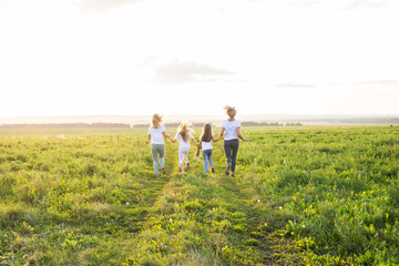 Fototapeta na wymiar Family, summer and holiday concept - Group of women and girls going away in green field