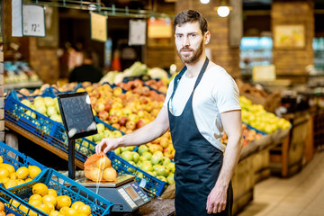 Portrait of a handsome worker weghing apples on the scales in the supermarket