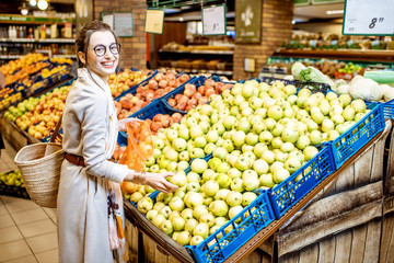 Young woman choosing apples to buy standing in the department with fruits and vegetables in the supermarket