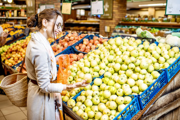 Young woman choosing apples to buy standing in the department with fruits and vegetables in the supermarket