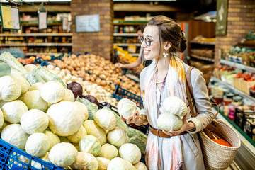 Young woman choosing cabbages to buy standing in the vegetable department in the supermarket
