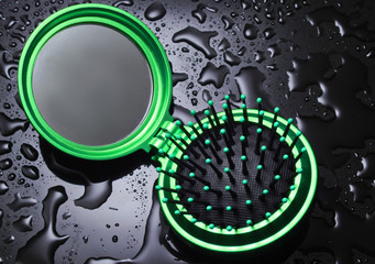 Mini pocket mirror hairbrush with water drops on a black background..