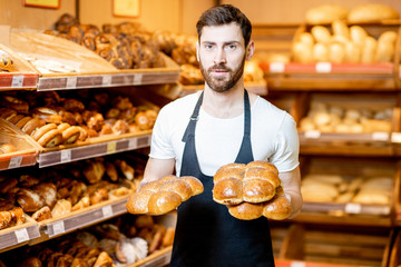 Portrait of a handsome baker in uniform standing with fresh pastries in the bakery deparment of the supermarket