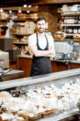 Portrait of a handsome seller in uniform standing near the showcase with cheese in the supermarket