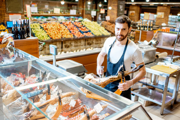 Handsome seller slicing jamon on the counter with dried meat in the supermarket