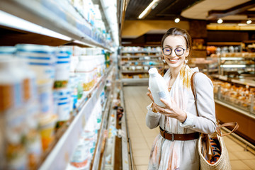 Fototapeta premium Young woman choosing milk standing near the shelves with dairy products in the supermarket