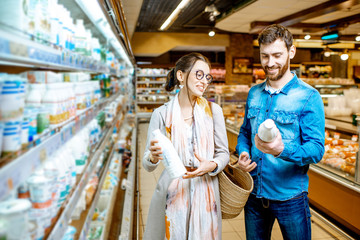 Young couple choosing milk standing together near the shelves with dairy products in the supermarket