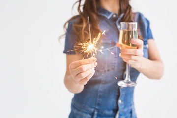 Celebration, drinks and holiday concept - close up of young woman with sparkler and glass of champagne on white background