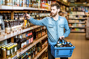 Man with thirst to alcohol taking beer from the shelves with strong drinks in the supermarket