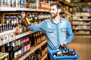 Man with thirst to alcohol taking beer from the shelves with strong drinks in the supermarket