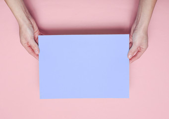 Female hands holding blue paper sheet on pink background. Top view. Mockup, copy space, minimalism