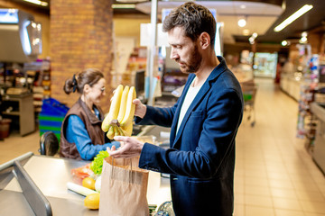 Businessman buying healthy food, packing products at the cash register with cheerful cashier in the supermarket