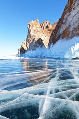 Lake Baikal in winter. Beautiful ice with lines of cracks near the coastal cliffs of Three Brothers (Sagan-Khushun) of Olkhon Island. Tourist photographer shoots huge icings and icicles on the rocks