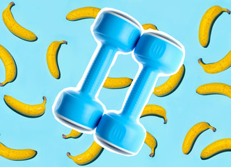 Two blue plastic dumbbells on background of bananas. Zine style, pop art, creative concept