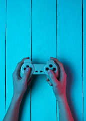 Concept gamer. Nightlife. Leisure. Hand holds gamepad on blue wooden background. Neon red blue...
