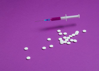 Medical minimalistic concept. Syringe, pills on purple background.