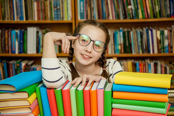 Happy girl in glasses with books in the library