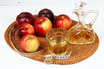Apple vinegar and apples. Fresh apples, apple vinegar, measuring tape, a bottle and glass on white wooden table