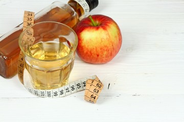 Apple vinegar and apples. Fresh apple, apple vinegar, measuring tape and glass on white wooden table
