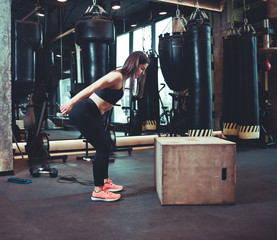 Fitness woman jumping on wooden box training at the gym, cross fit workout. Brunette girl in sportwear doing some jumping exercises in gym