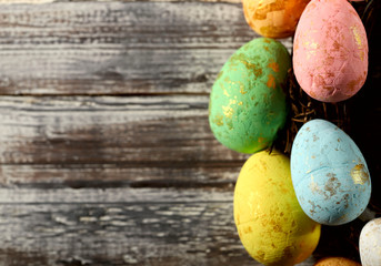 Easter background. Right on a brown wooden background are yellow, orange, green, blue and pink painted eggs with gold stains. Free space in the center for text. The concept of religion and tradition.