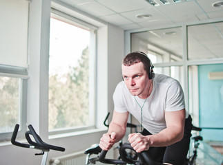 Fototapeta na wymiar Healthy lifestyle concept. Young sporty man in white t-shirt and shorts is exercising bike at spinning class . Cardio training