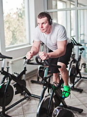 Naklejka na ściany i meble Healthy lifestyle concept. Young sporty man in white t-shirt and shorts is exercising bike at spinning class . Cardio training