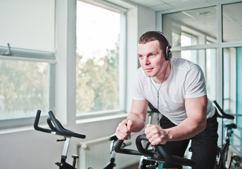 Naklejka na ściany i meble Healthy lifestyle concept. Young sporty man in white t-shirt and shorts is exercising bike at spinning class . Cardio training
