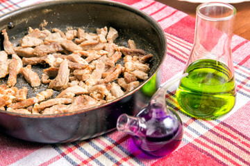 Slices of fried meat in a frying pan. Nutritional supplements. Flask and beaker with chemical liquids