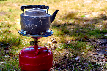 Close up of boilng old kettle on the portable camping gas stove with red propane balloon