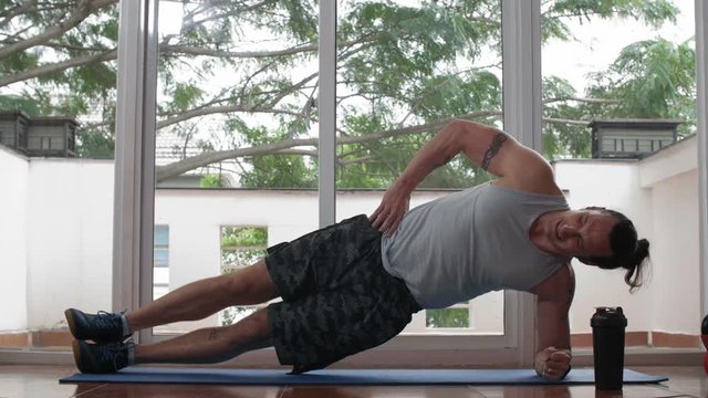 Wide shot of Caucasian sporty man doing side plank position in gym