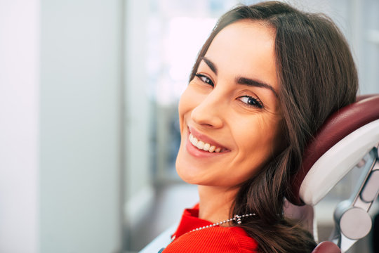 Dental Surgery. Dental chair in the stomatology cabinet with the bodacious girl in it, who is clothed in  a red sweater. Her teeth are white and healthy and she is happy about that.