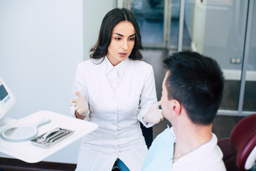 Fototapeta premium What are your complaints? A dentist on her work in the hospital is sitting right in front of a patient in medical clothes and asking about his complaints.