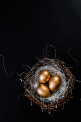 Golden Easter Eggs in birds Nest on black background. Easter Holiday concept abstract background copyspace top view several objects.