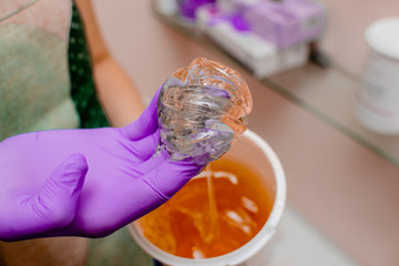 Wax bar with sugar paste depilation and beauty concept - sugar paste or wax honey for hair removing with bright  purple gloves hands of cosmetologist in spa salon. Top view several objects