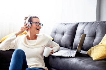 Obraz premium Attractive woman in her room with laptop and coffe mug on her hand with headphones over her head