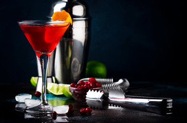 Classic alcoholic cocktail cosmopolitan with vodka, liqueur, cranberry juice, lime, ice and orange zest, dark bar counter background, night mood, space for text