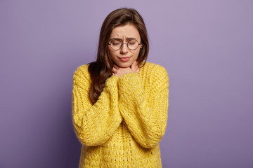 Cold again. Upset woman feels inflammation, keeps eyes shut, feels discomfort caused by illness, has sore throat, unable to give speech, worries about health, wears yellow sweater, stands indoor