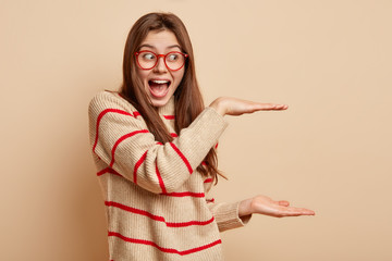 Photo of cheerful woman boasts of present size she received, shapes big object with both hands,...