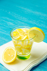 Water with lemon. Lemonade with lemon slices on blue wooden background.